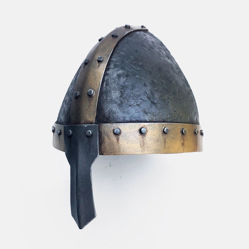 May include: A dark gray helmet with a gold band and metal rivets. The helmet has a pointed metal nose guard.