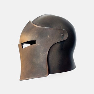 May include: A brown metal helmet with a face shield. The helmet has a rounded top and a pointed chin guard. The helmet is made of metal and has a weathered finish.