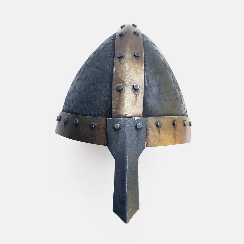 May include: A black and gold Viking helmet with a pointed nose guard. The helmet is made of metal and has a textured surface.