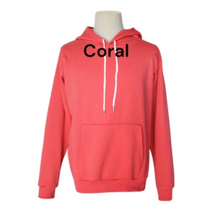 May include: A coral colored hoodie with a white drawstring and a kangaroo pocket. The word "Coral" is printed in black on the front of the hoodie.