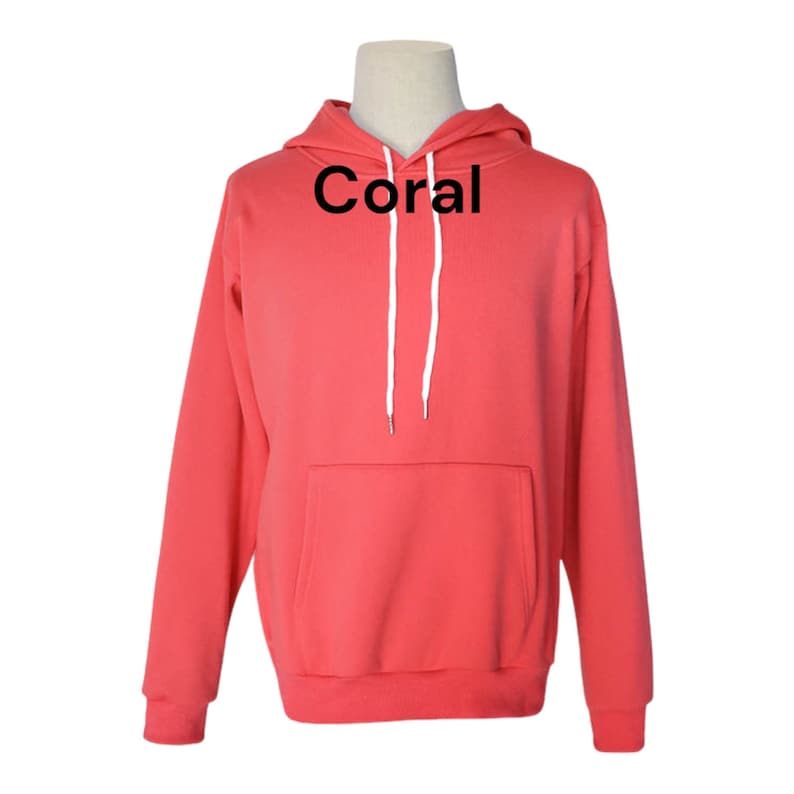 May include: A coral colored hoodie with a white drawstring and a kangaroo pocket. The word "Coral" is printed in black on the front of the hoodie.
