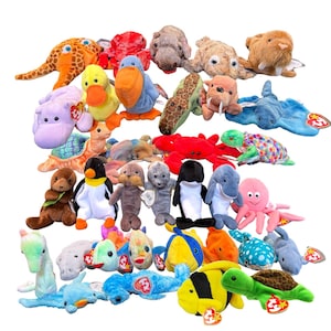 Puede incluir: Una colección de peluches de criaturas marinas, incluyendo una jirafa, un pato, un cangrejo, una tortuga y un pulpo. Los animales de peluche son de varios tamaños y colores, con etiquetas adjuntas.