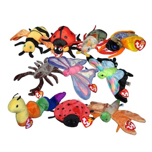 May include: A selection of soft toy insects, including a ladybug, butterfly, bee, and caterpillar. The toys are brightly coloured with various patterns and textures. Each toy has a small heart-shaped tag attached.