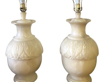May include: A pair of alabaster lamps with carved leaf details. The lamps have a cream-colored finish and gold-toned hardware.