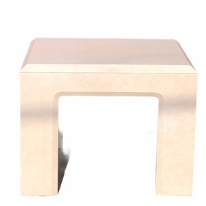 May include: A white, square end table with a simple, modern design. The table has a smooth, flat top and a rectangular base with an open, rectangular space in the center.