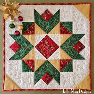 May include: A quilted table runner featuring a starburst design in red, green and gold fabrics. The runner is edged with a red and white checked trim. The text "Helle-May Designs" is visible in the bottom right corner.