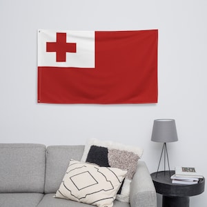 Könnte beinhalten: Eine rote Flagge mit einem weißen Kreuz in der oberen linken Ecke. Die Flagge hängt an einer weißen Wand über einem grauen Sofa mit Kissen.
