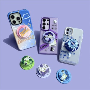 May include: Three smartphones with decorative cases and matching pop sockets. One case is blue with clouds and the text "Sweet Dreams". Another is purple with the text "Layolv". The third is gray with the text "Indigo".