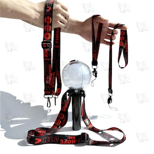 Könnte beinhalten: Ein schwarzes und rotes Schlüsselband-Set mit einer leuchtenden Kugel. Die Schlüsselbänder haben Text in Rot und Schwarz, mit einem schwarzen verstellbaren Riemen und einem Metallverschluss. Die Kugel ist transparent mit einem schwarzen Sockel.