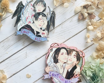 Puede incluir: Dos pines de esmalte con ilustraciones de parejas. Un pin muestra una pareja con alas de ángel y el texto "LOVEWINSALL" en una pancarta azul. El otro pin muestra una pareja abrazándose con el texto "LOVEWINSALL" en una pancarta rosa.