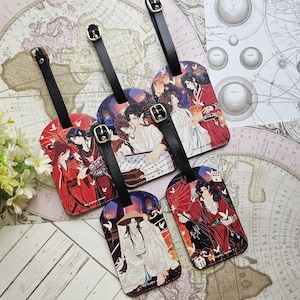 Könnte beinhalten: Fünf rechteckige Kofferanhänger mit Anime-Illustrationen von Figuren in traditioneller ostasiatischer Kleidung. Jeder Anhänger verfügt über einen schwarzen Lederriemen mit einer silbernen Metallschnalle in den Farben Rot, Weiß und Schwarz.