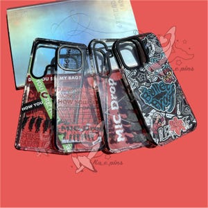 Könnte beinhalten: Vier transparente Handyhüllen mit schwarzen Rändern, die verschiedene grafische Designs und Text aufweisen. Die Designs enthalten die Wörter "MIC Drop", "How You" und "Bulletproof". Die Hüllen liegen auf einer roten Oberfläche mit einem Buch im Hintergrund.