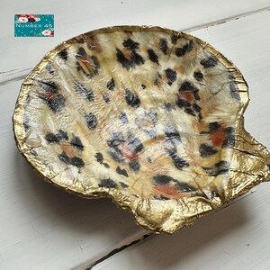 May include: A decorative, shell-shaped dish with a leopard print pattern in tan, black, and red. The rim is trimmed with gold foil. The dish is on a white surface. The text "NUMBER 45" is in the upper left corner.