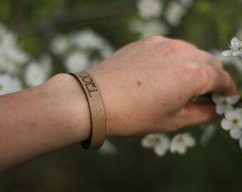 Puede incluir: Una pulsera de cuero marrón con el nombre "JOEL" grabado.
