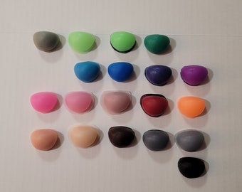 May include: Assortment of 20 small, round, colourful resin cabochons. The cabochons are arranged in rows on a white surface. The colours include pink, green, blue, purple, red, orange, brown, grey, and black.