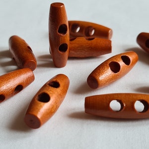 May include: A group of eight brown wooden toggle buttons, each with two holes. The buttons are oval shaped and have a smooth finish.