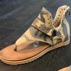 May include: Camouflage print sandals with a buckle and gold studs. The sandals have a brown leather sole and a toe thong.