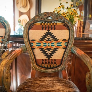 May include: Two ornate wooden chairs with a Southwestern-style patterned fabric upholstery. The chairs have a distressed paint finish and are decorated with gold accents. The chairs are set against a backdrop of a wooden bar with a granite countertop.