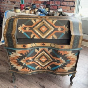May include: A vintage secretary desk with a dark brown finish and a geometric pattern in shades of orange, blue, and gold. The desk has a curved front and a roll-top lid.