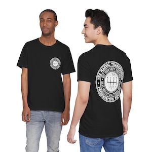 May include: A black short-sleeve t-shirt featuring a white circular graphic on the left chest and a larger version on the back. The graphic displays a manual transmission gear shift pattern with the text THE MANUAL TRANSMISSION PRESERVATION SOCIETY.