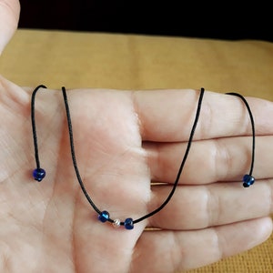 May include: A simple necklace with a black cord and three beads. Two of the beads are blue and one is silver.