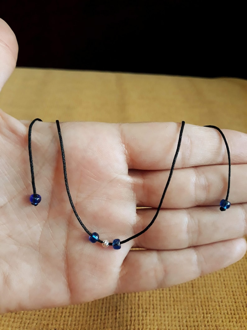 May include: A simple necklace with a black cord and three beads. Two of the beads are blue and one is silver.