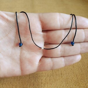 May include: A simple black cord necklace with two small blue beads and a silver bead in the center.