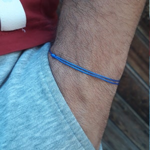 Puede incluir: Un brazalete de cuerda azul usado en la muñeca.