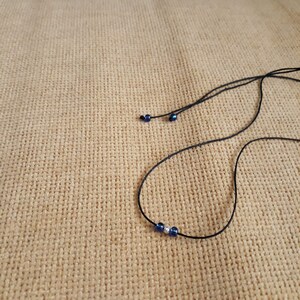 May include: A simple necklace with a black cord and three beads, two blue and one silver.