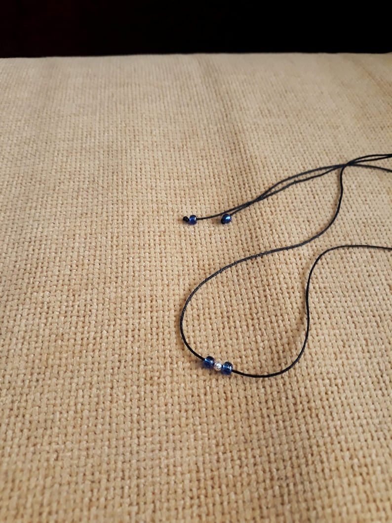May include: A simple necklace with a black cord and three beads, two blue and one silver.