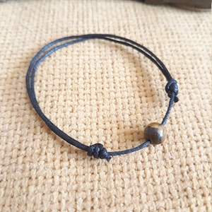 May include: A black string bracelet with a brown and black bead.