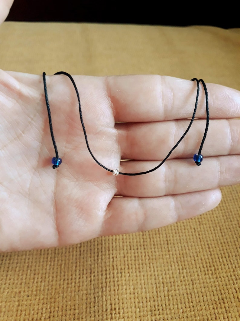 May include: A simple black cord necklace with two small blue beads and a silver bead in the center.