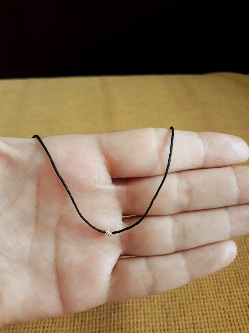 May include: A simple black cord necklace with a small silver bead accent.