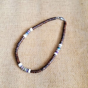 Puede incluir: Un collar de cuentas de madera marrón con detalles blancos y morados. El collar tiene un cierre plateado.