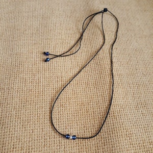 May include: A black cord necklace with two small blue beads at the end and three blue beads in the center.