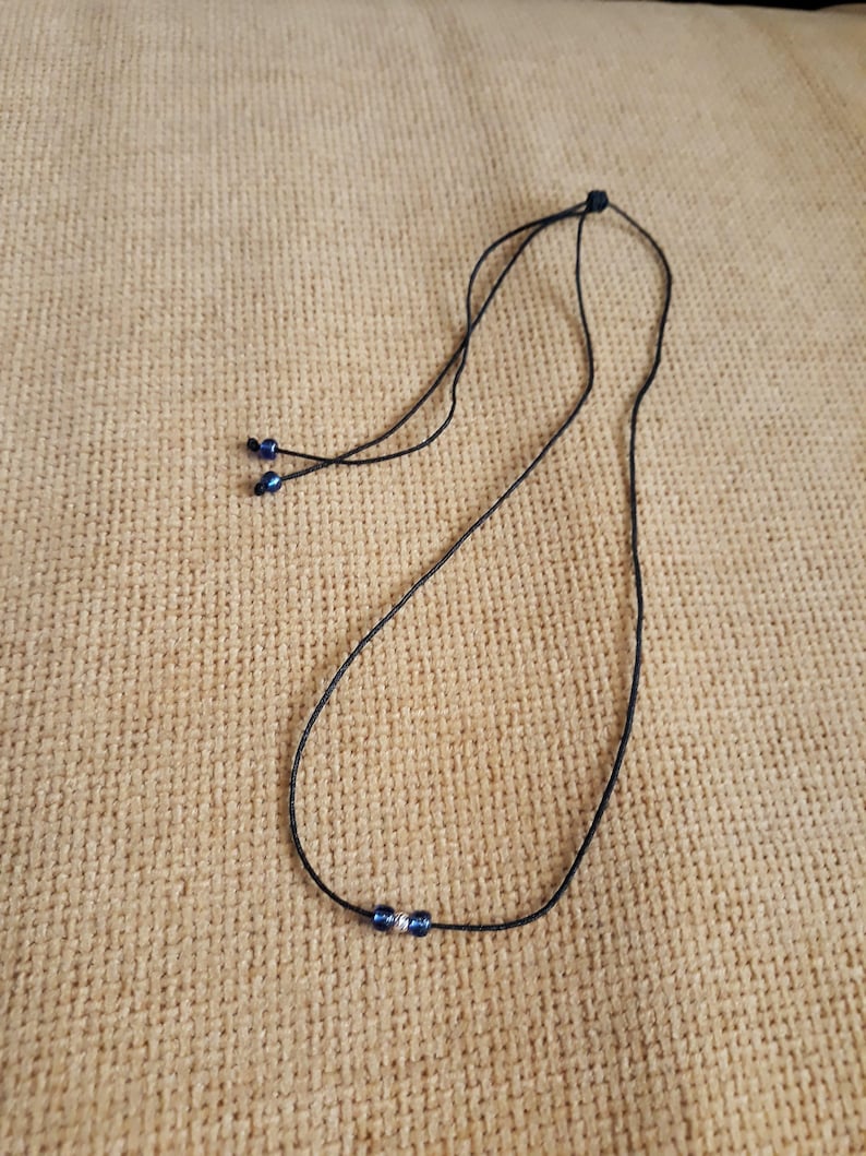 May include: A black cord necklace with two small blue beads at the end and three blue beads in the center.