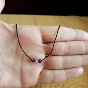May include: A simple necklace with a black cord and three beads. The beads are blue and silver.