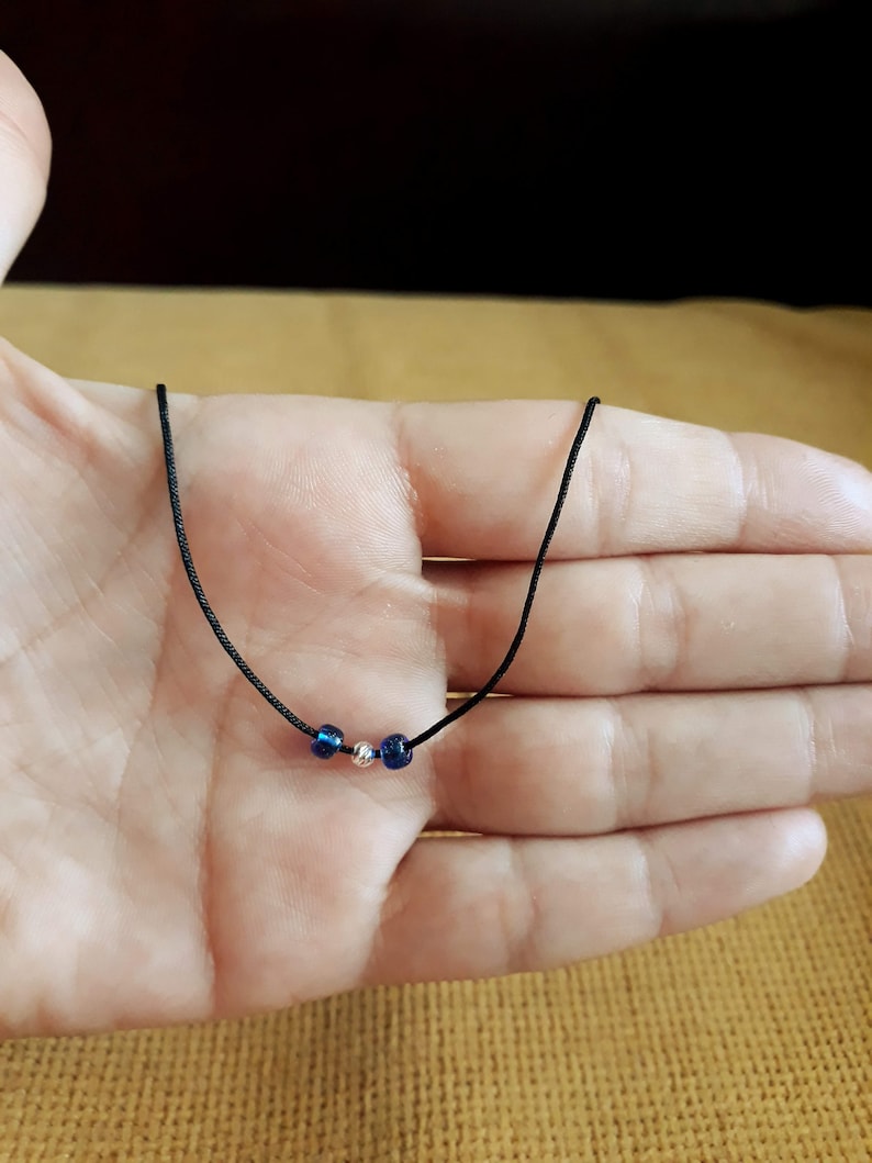 May include: A simple necklace with a black cord and three beads. The beads are blue and silver.