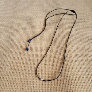 May include: A simple black cord necklace with a small silver bead pendant.