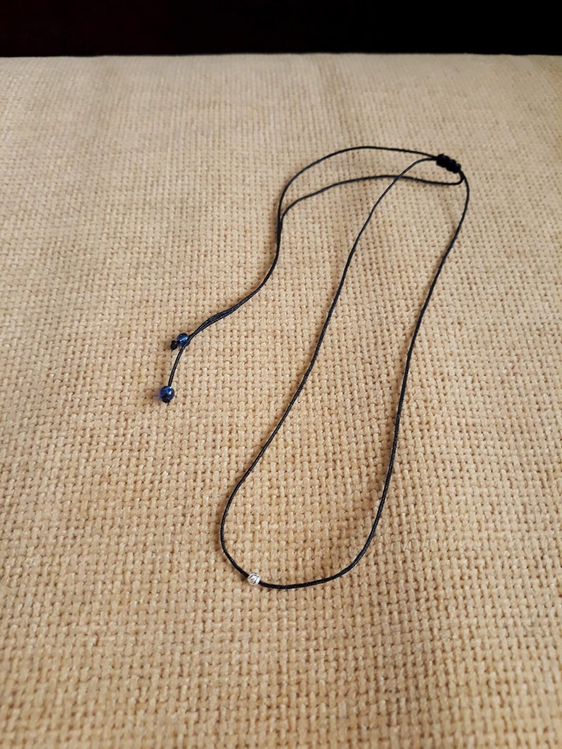 May include: A simple black cord necklace with a small silver bead pendant.
