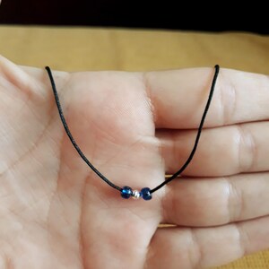 May include: A simple necklace with a black cord and three beads. Two of the beads are dark blue and one is silver.