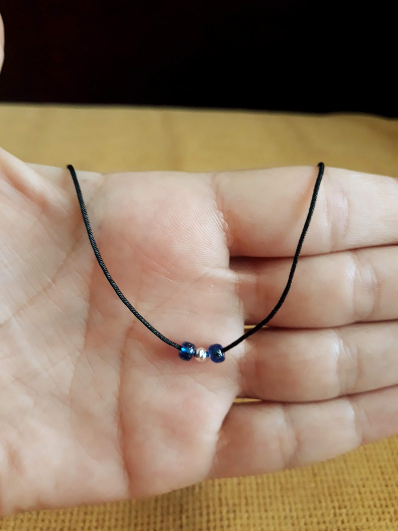 May include: A simple necklace with a black cord and three beads. Two of the beads are dark blue and one is silver.