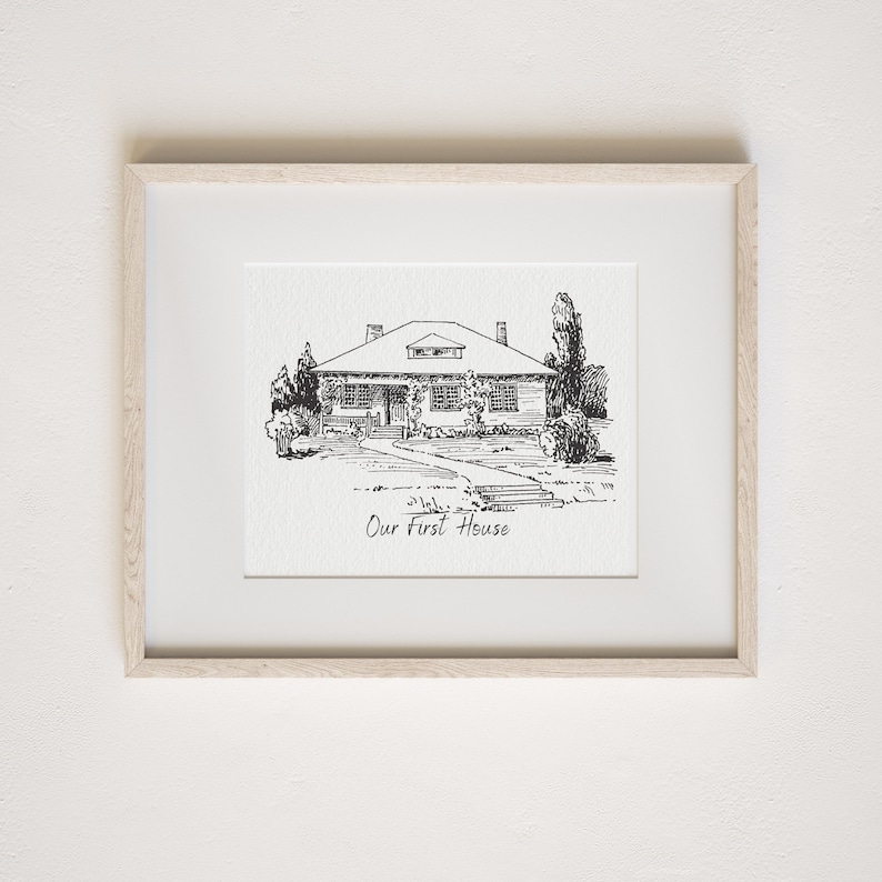 Op de afbeelding: Een zwart-witte lijntekening van een huis met een voorporch en een pad dat naar de voordeur leidt. De tekening is ingelijst in een licht houten lijst en de tekst "Our First House" staat onder de tekening.