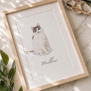 May include: A framed watercolor illustration of a white cat with grey tabby markings on its head and tail. The cat is sitting in a centered position. Below the cat, the name Mallow is written in a black cursive script on the white paper.