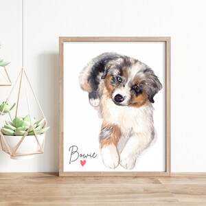May include: Watercolor painting of a blue merle Australian Shepherd puppy with brown markings. The puppy is sitting with its head tilted and looking at the viewer. The painting is framed in a light wood frame and has the name "Bowie" written below the puppy with a red heart.