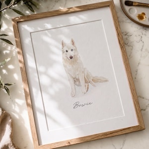 May include: A framed watercolor portrait of a white dog sitting down, featuring the name Bowie written in black cursive script below the illustration. The artwork is encased in a light-toned wooden frame with a white mat border.