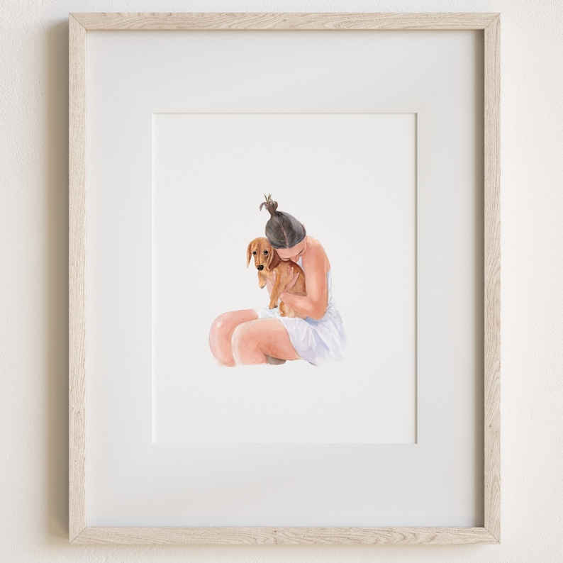 May include: A framed watercolor illustration featuring a person with dark hair tied in a top knot, wearing a white sleeveless garment, sitting and embracing a small brown dachshund dog. The artwork is encased in a light-toned wooden frame.
