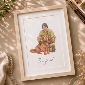 May include: A framed watercolor illustration featuring a person wearing a dark beanie and a tan jacket kneeling beside a golden-colored dog. The artwork is set within a light-colored wooden frame and includes the handwritten text True friend.