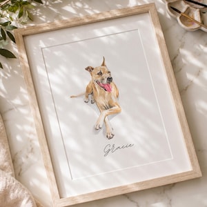 May include: A framed watercolor portrait of a tan dog with its tongue out, lying down with crossed front paws. The name Gracie is written in black cursive script below the dog. The artwork is enclosed in a light-colored wooden frame.