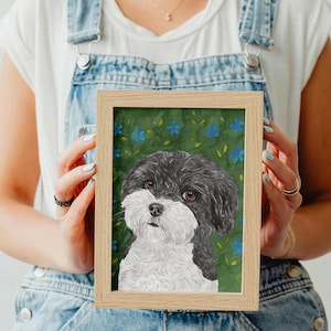 以下が含まれることがあります： ふわふわした毛並みの白黒の犬の肖像画が、小さな青い花と緑の葉が描かれたダークグリーンの背景に飾られています。このアートワークは、シンプルで清潔感のある縁取りの明るい木製フレームに収められています。